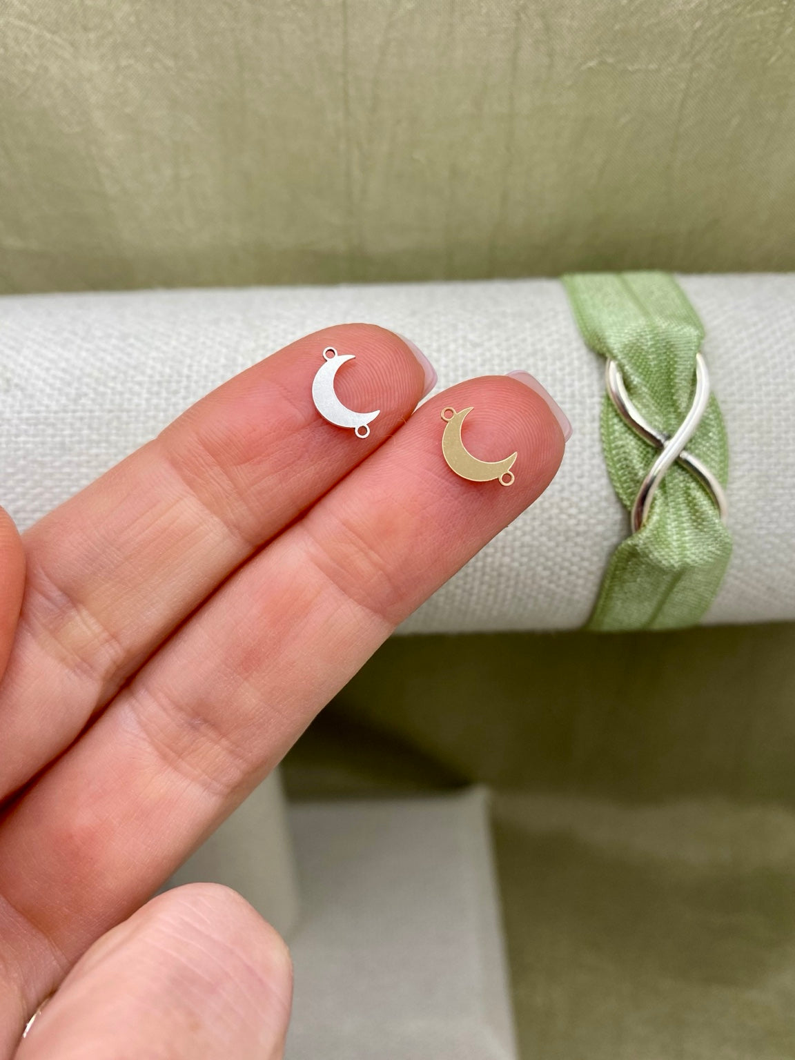 Sterling silver and gold-filled crescent moon connectors on fingertips beside a green ribbon bracelet